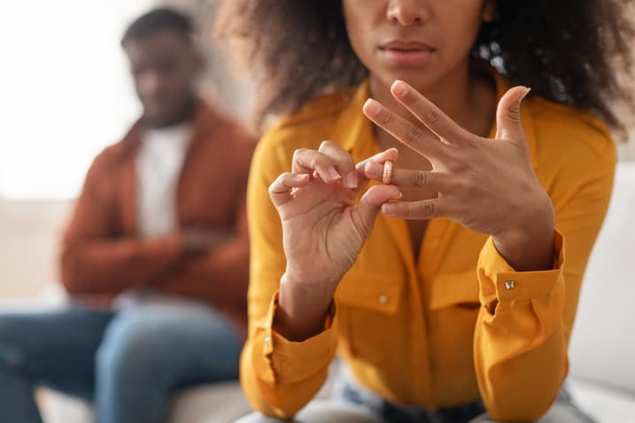 Woman removing her wedding ring while sitting apart from her partner