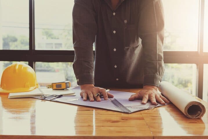Builder reviewing house plans with tools and hard hat on table