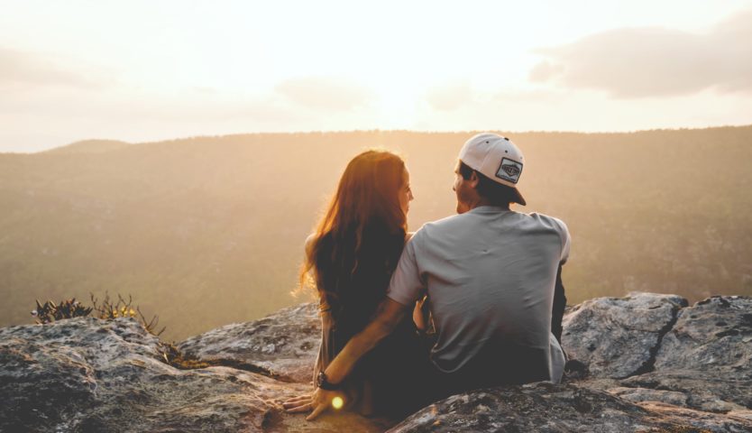 young couple sitting on hill enjoying sunset