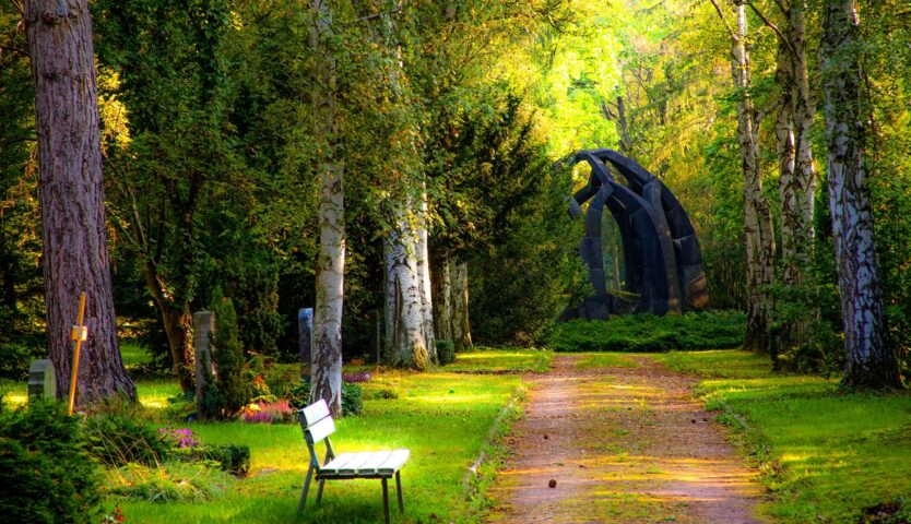 lush graveyard with stone arch and bench along side of path