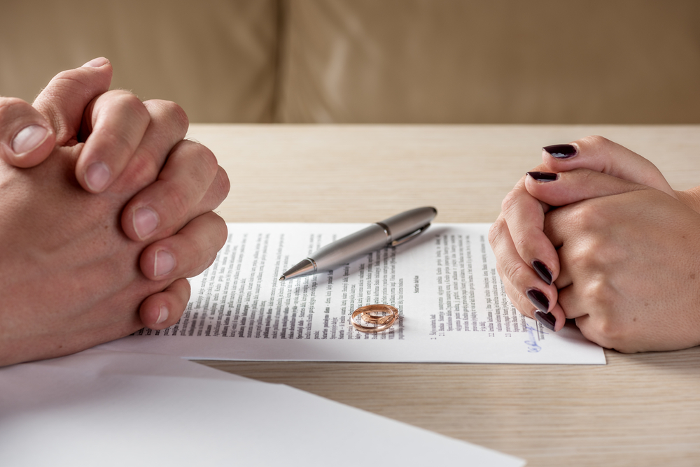 hands clasped over signed divorce papers with pen and rings