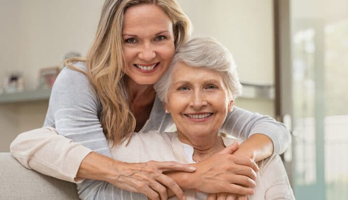 Adult daughter hugging elderly mother while sitting together at home