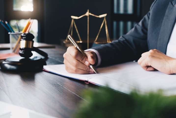 Lawyer signing legal documents at desk with gavel and scales of justice