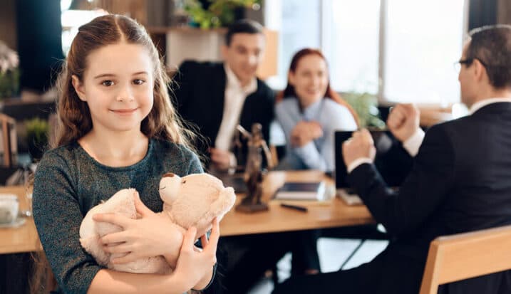 Child holding teddy bear while parents meet with lawyer about guardianship