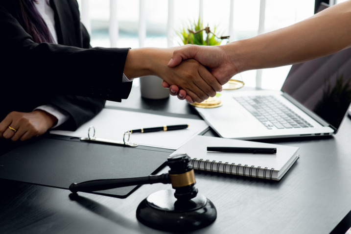 Client and lawyer shaking hands across desk with gavel and documents