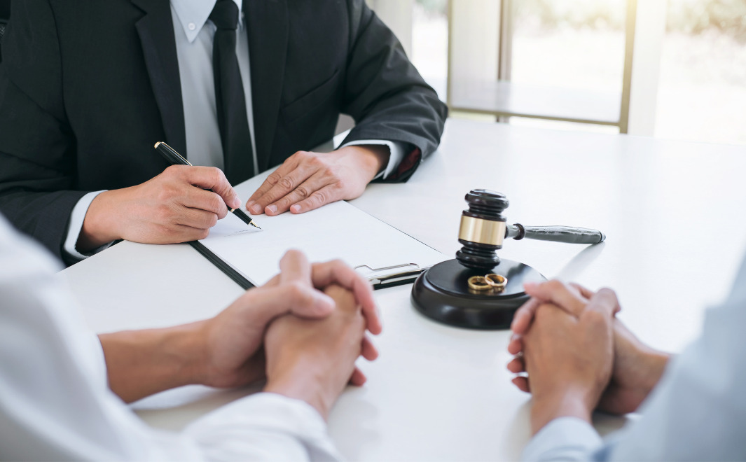 Lawyer reviewing separation documents with couple seated across the table and wedding rings beside a gavel